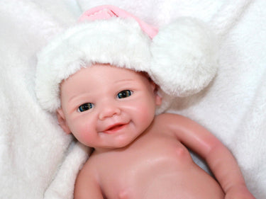 A baby doll wearing a pink and white outfit, featuring a sweet expression and soft, cuddly features.